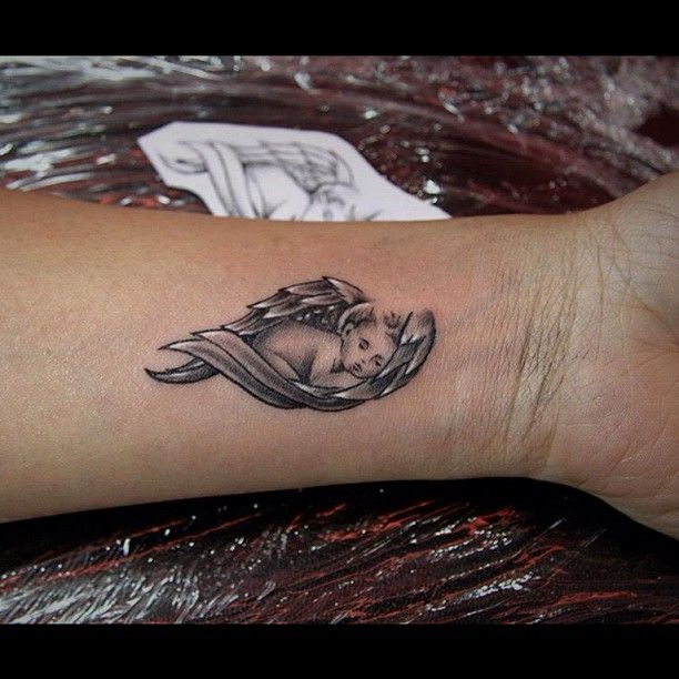 Black Ink Sleeping Baby Angel Tattoo On Left Wrist