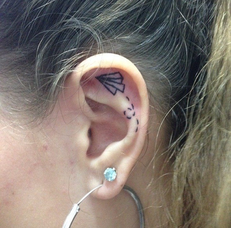 Black Outline Paper Plane Tattoo On Girl Left Ear
