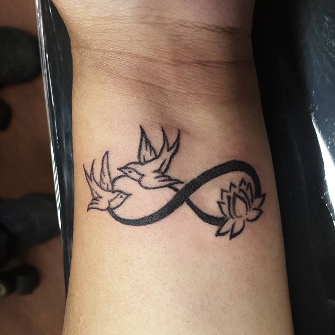 Black Infinity With Lotus Flower And Flying Birds Tattoo On Wrist