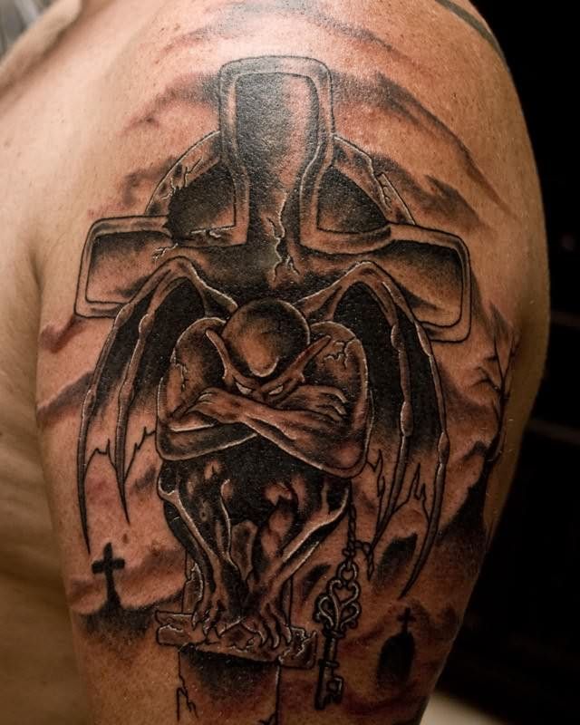 Black Ink Cross With Gargoyle Tattoo On Man Left Shoulder