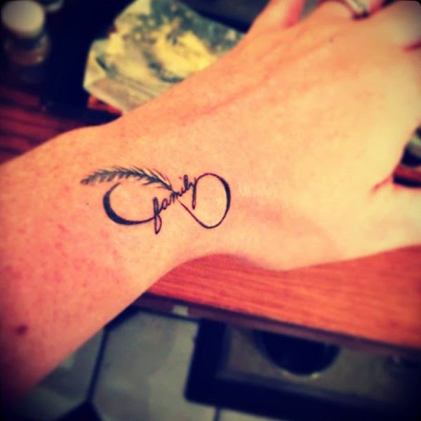 Black Ink Infinity With Feather Tattoo On Left Upper Wrist