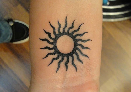 Black Outline Simple Sun With Tribal Rays Tattoo On Wrist