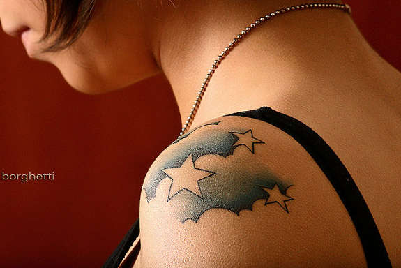 Tatuajes de nubes azules y estrellas en el hombro izquierdo de una chica