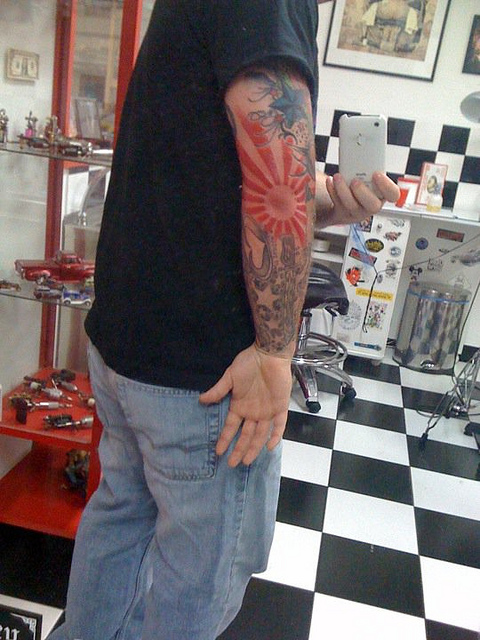 Man With Rising Sun Tattoo On Right Sleeve
