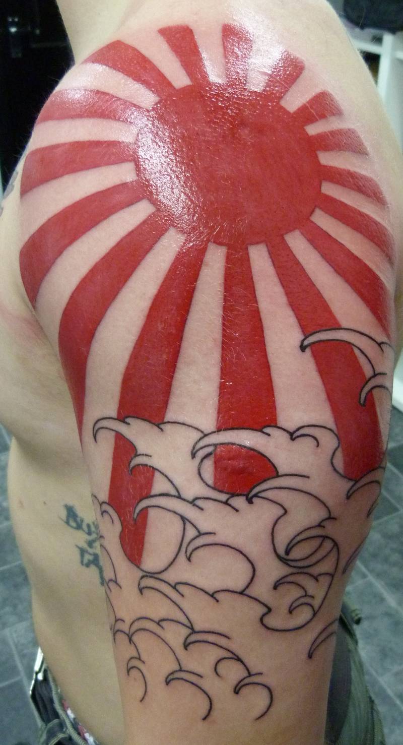Outline Water Waves And Red Ink Rising Sun Tattoo On Man Left Shoulder