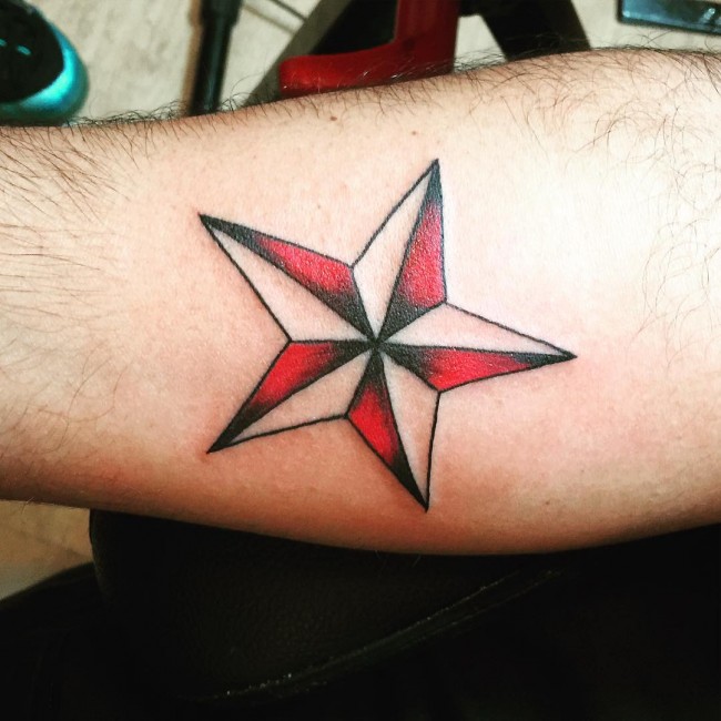 Tatuaje de estrella náutica roja y negra en el antebrazo derecho