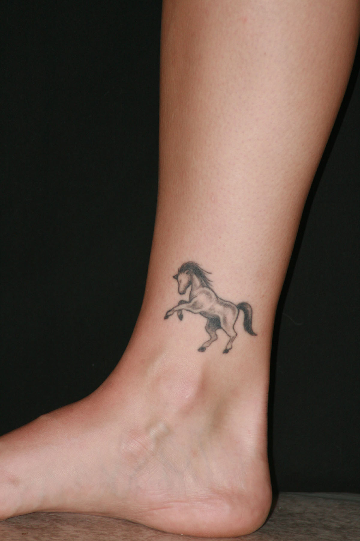 Grey Ink Running Horse Tattoo On Side Ankle