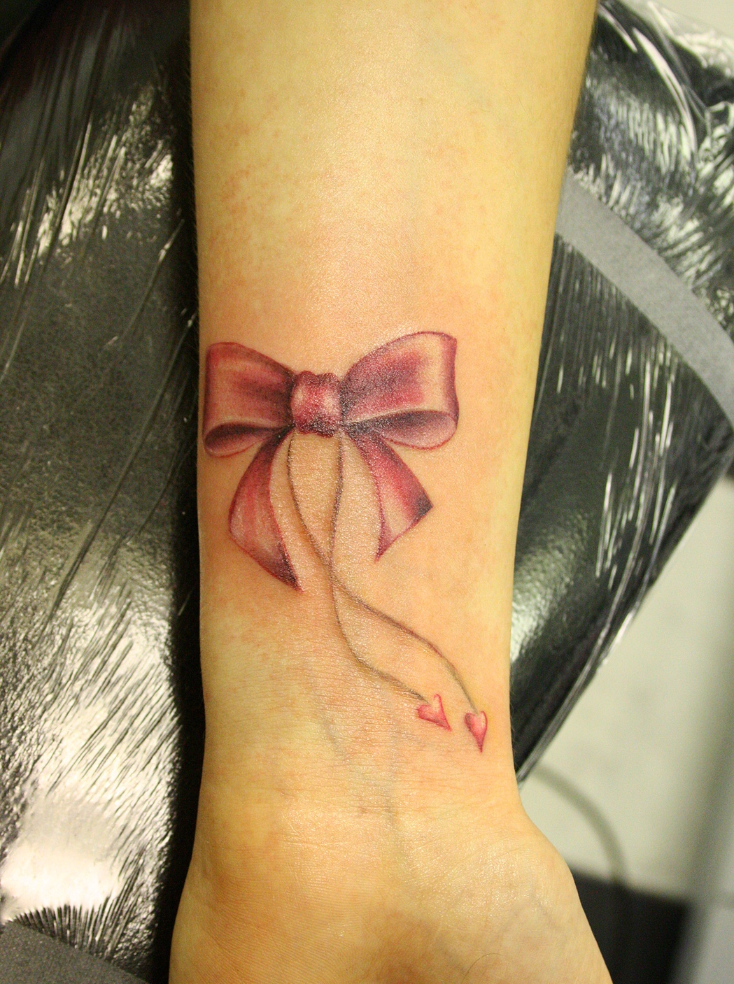 Pink Bow Tattoo On Girl Left Forearm