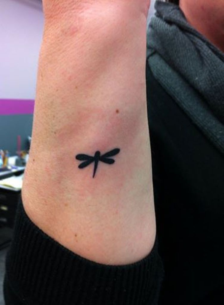 Tiny Black Ink Silhouette Dragonfly Tattoo On Forearm