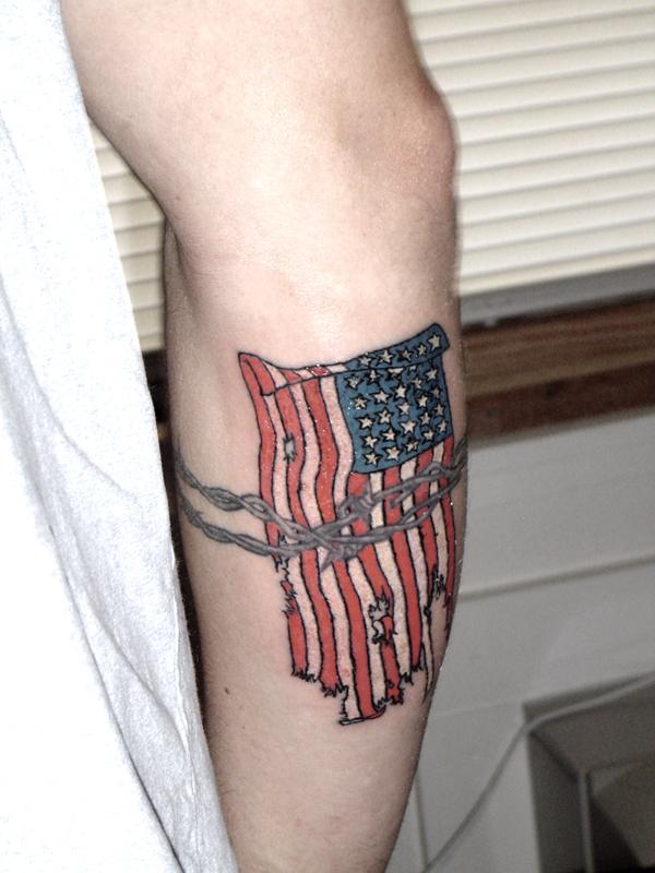 Tattered American Flag With Barbed Wire Tattoo On Arm