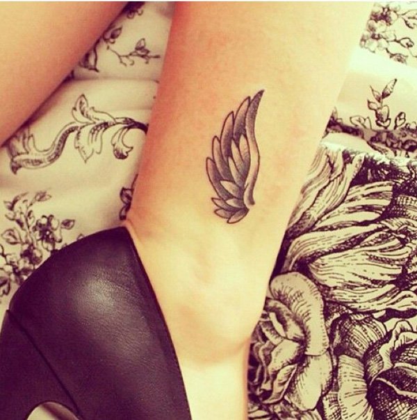 Grey Angel Wing Tattoo On Ankle Of An Angel