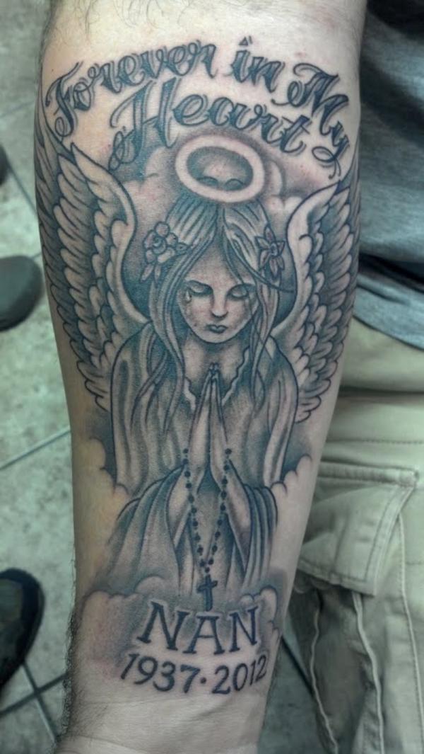 Grey Ink Holy Praying Angel Memorial Tattoo With Wording ‘Forever In My Heart’ On Forearm