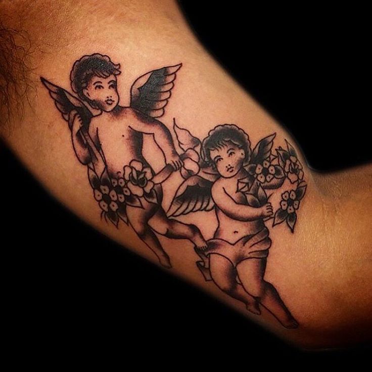 Two Cute Flying Angelic Cherubs With Flowers Tattoo On Bicep