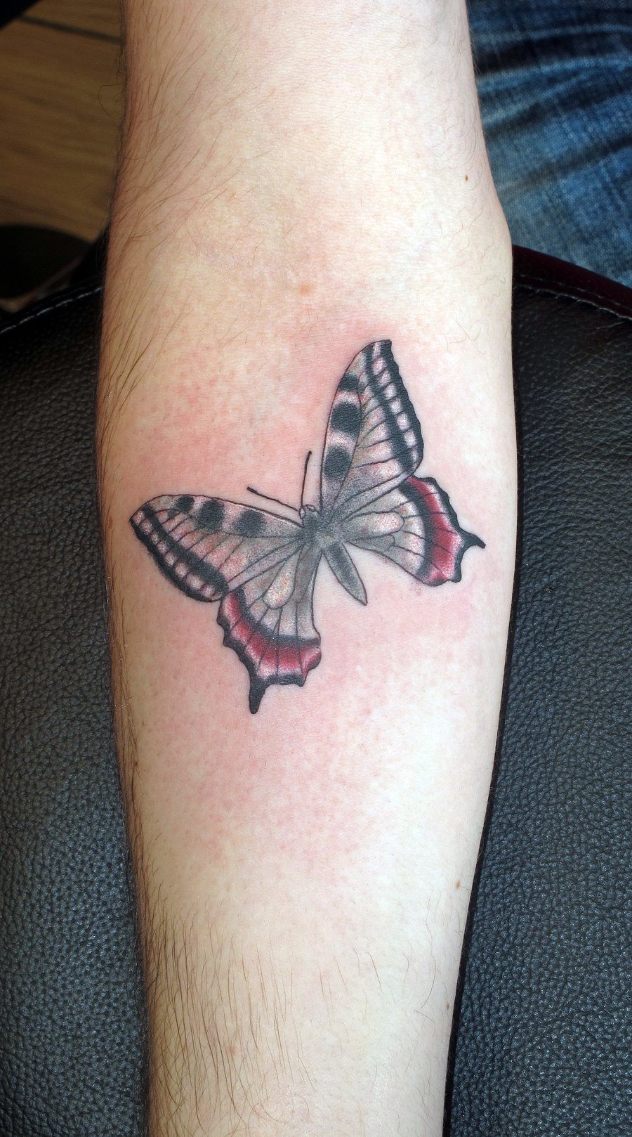 Black and red tribal butterfly tattoo on inner arm