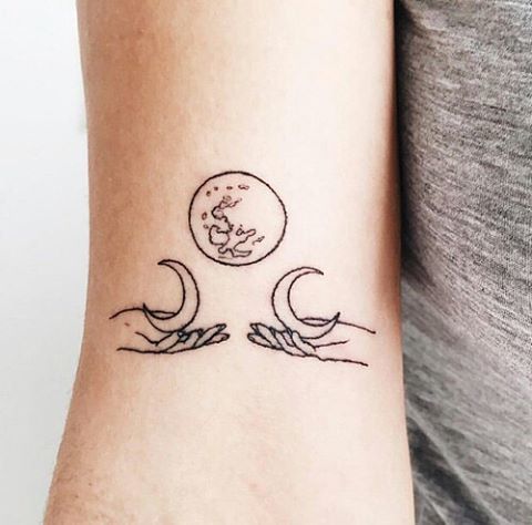 Black outlined earth and moons with hands tattoo on arm