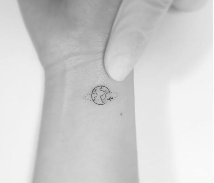 Black outlined small earth with airplane tattoo on wrist
