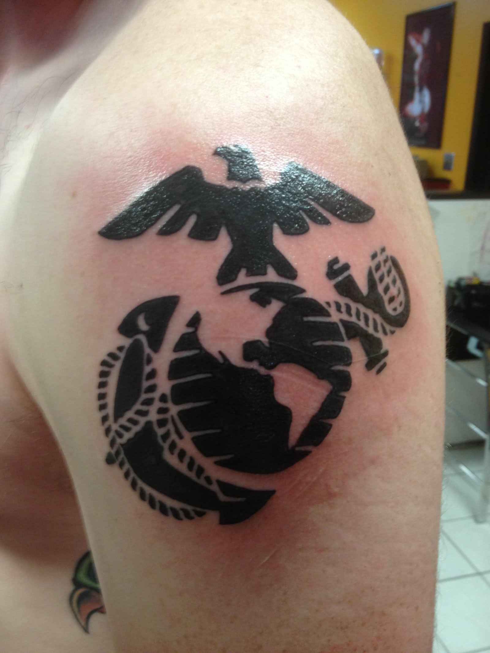 Black tribal globe, eagle and anchor tattoo on left upper arm