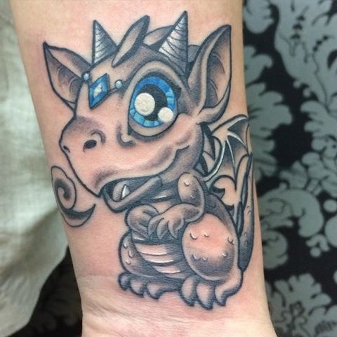 Blue and black baby dragon tattoo with innocent eyes on inner arm