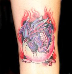 Colored flaming baby dragon tattoo coming out of egg on arm