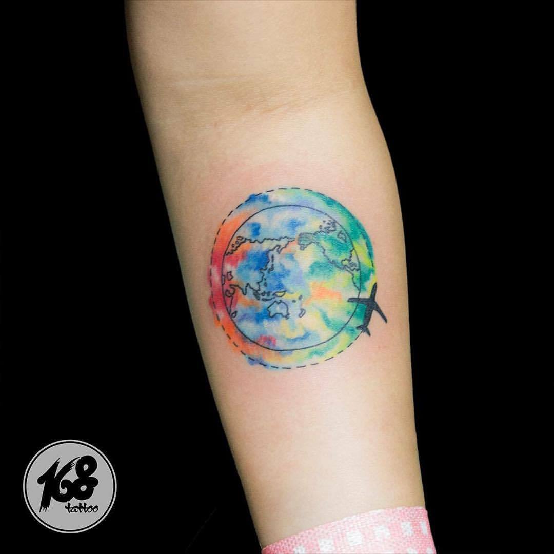 Colorful watercolor globe and airplane tattoo on inner arm