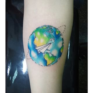 Colourful watercolour globe and airplane tattoo on inner forearm