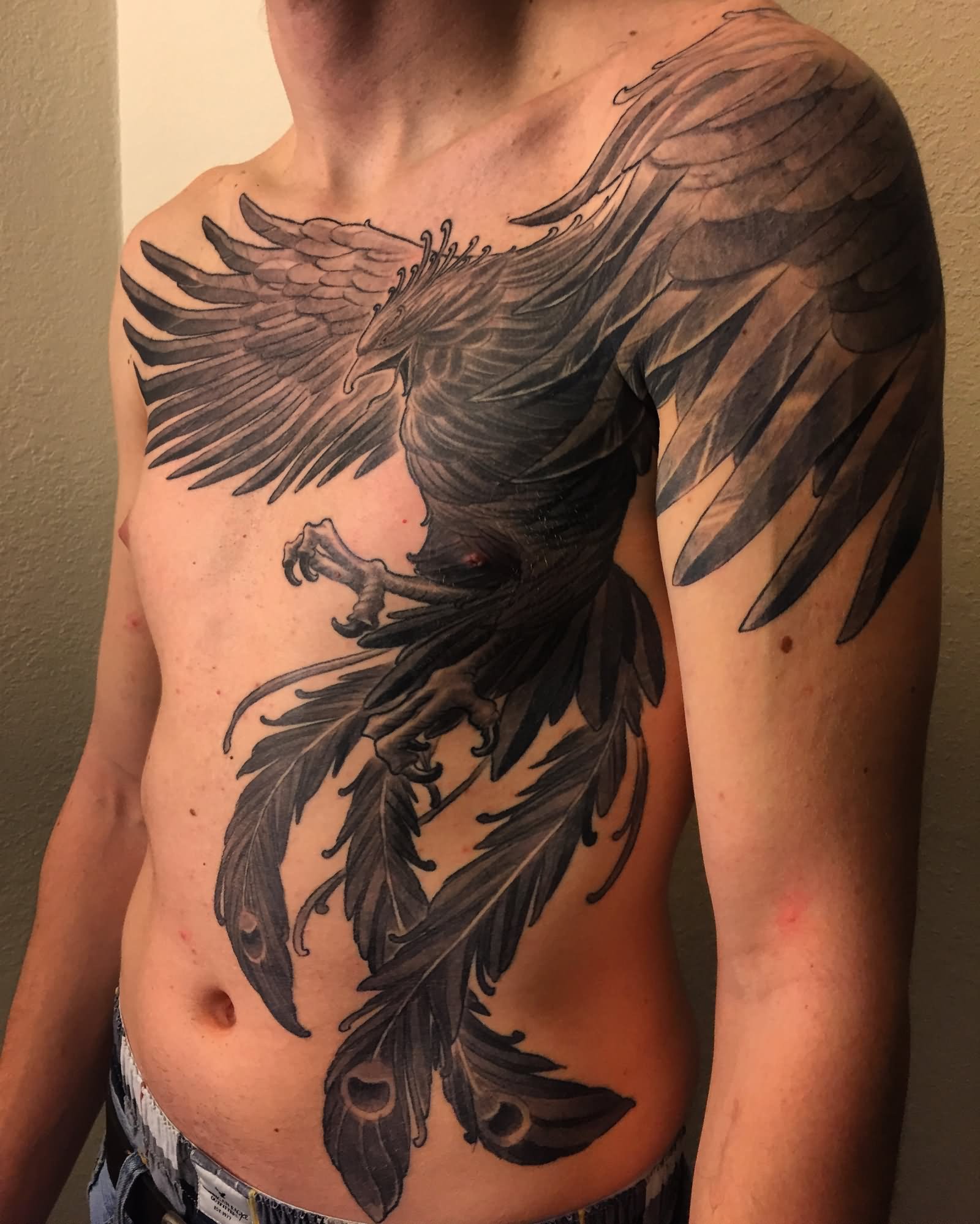 Large black ink phoenix tattoo on man front body and shoulder
