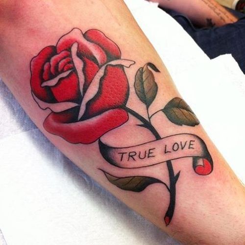 Open red rose and the inscription true love tattoo on outer forearm