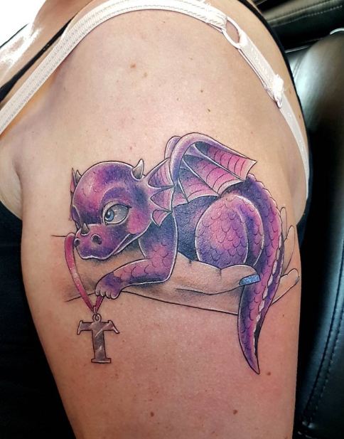 Purple baby dragon tattoo with hand and Celtic cross on left upper arm