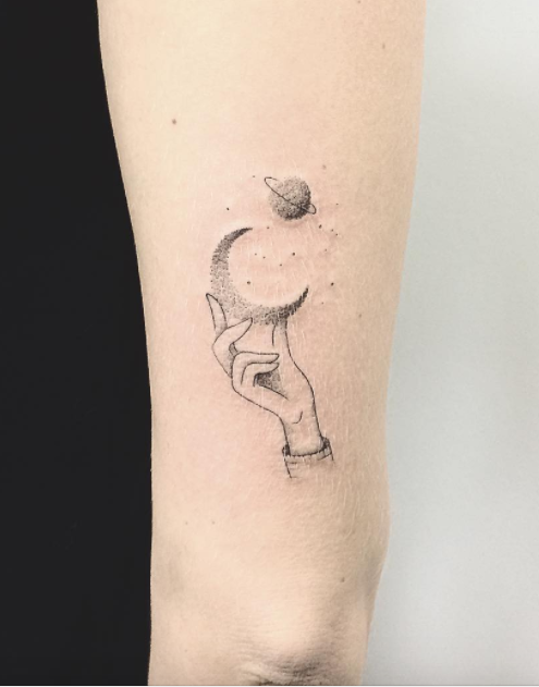 Black hand holding half moon and earth tattoo on arm