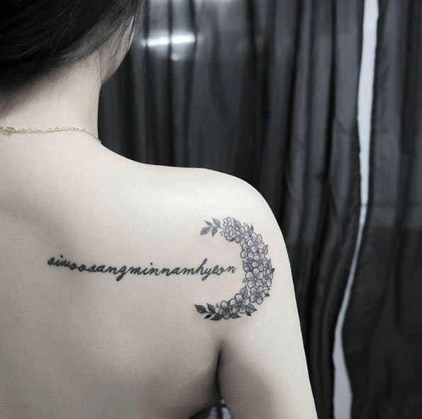 Black shaded half moon floral tattoo with text on right upper back for women