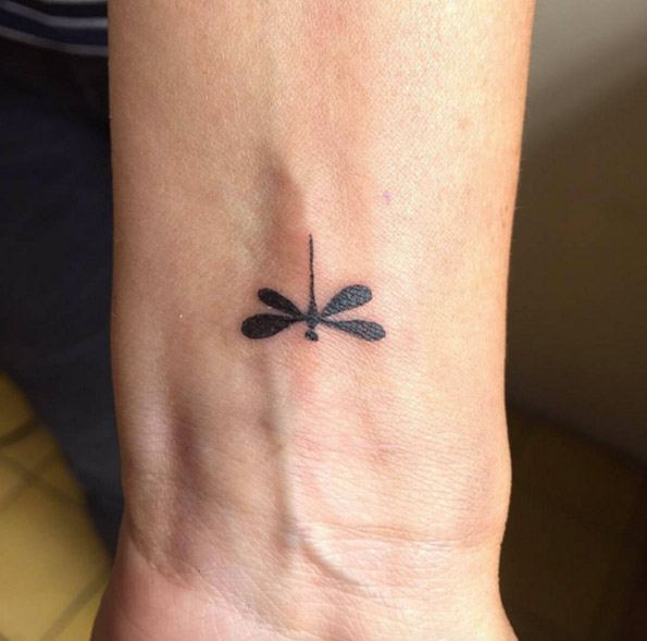 Black small dragonfly tattoo on inner arm below wrist