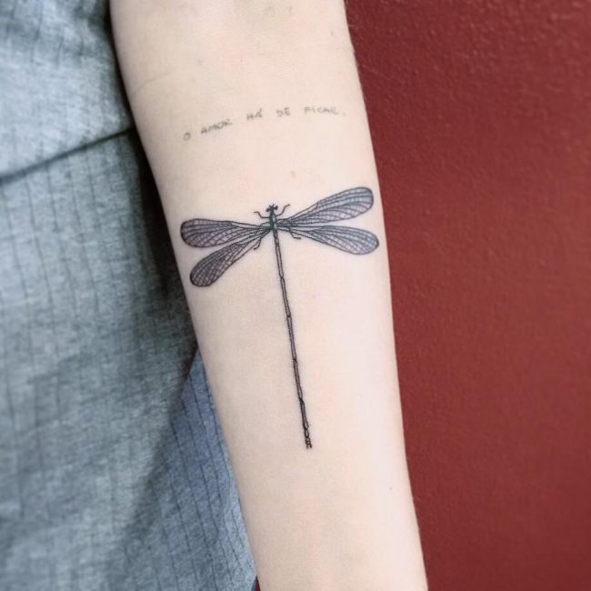 Black tribal dragonfly tattoo on girl’s inner arm