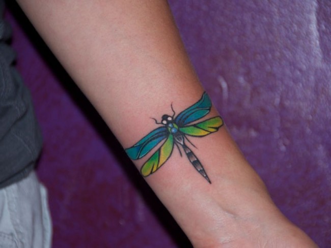 Colorful tribal dragonfly tattoo on inner lower arm