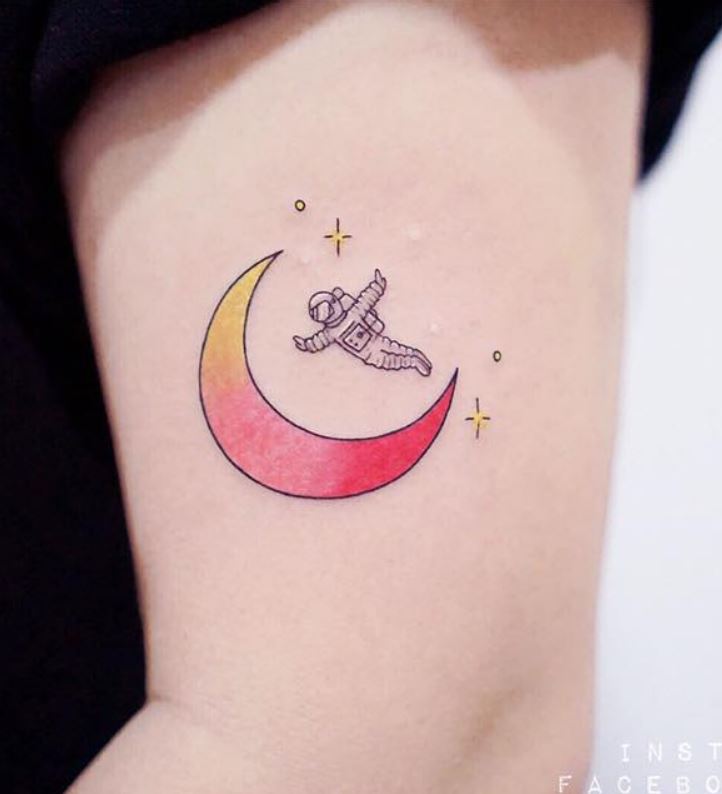 Red and yellow astronaut and half moon tattoo on left upper arm