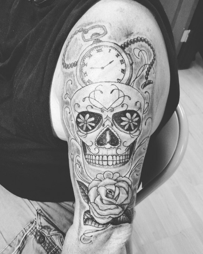 Black sugar skull with rose and stopwatch tattoo on upper arm