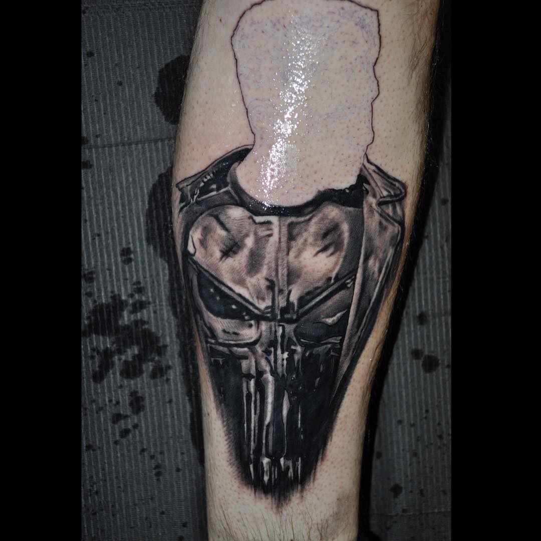 Black and grey shaded man and punisher skull tattoo on body