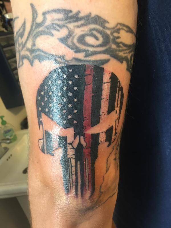 Black and red American flag punisher skull tattoo above elbow.