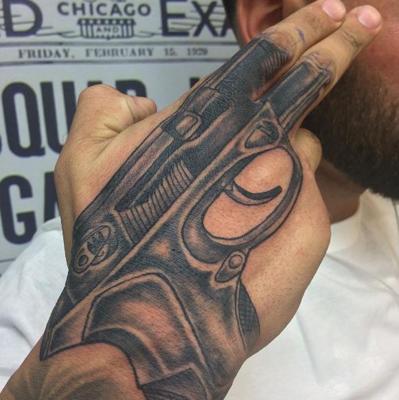 Grey shaded gun tattoo on upper right hand