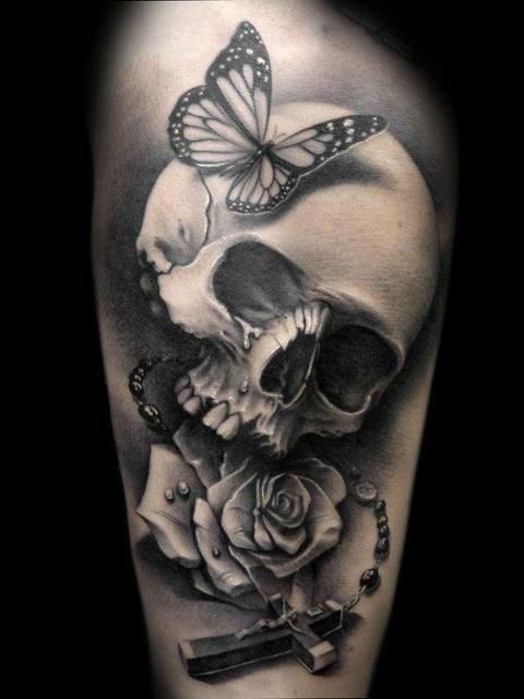 Black and white skull and rose with Celtic cross and butterfly tattoo on upper arm