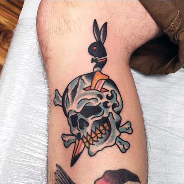 Blue and black traditional skull with knife tattoo on lower leg