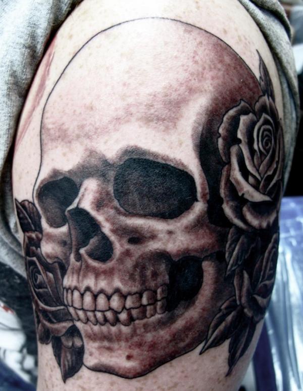 Grey shaded skull and roses tattoo on upper left arm