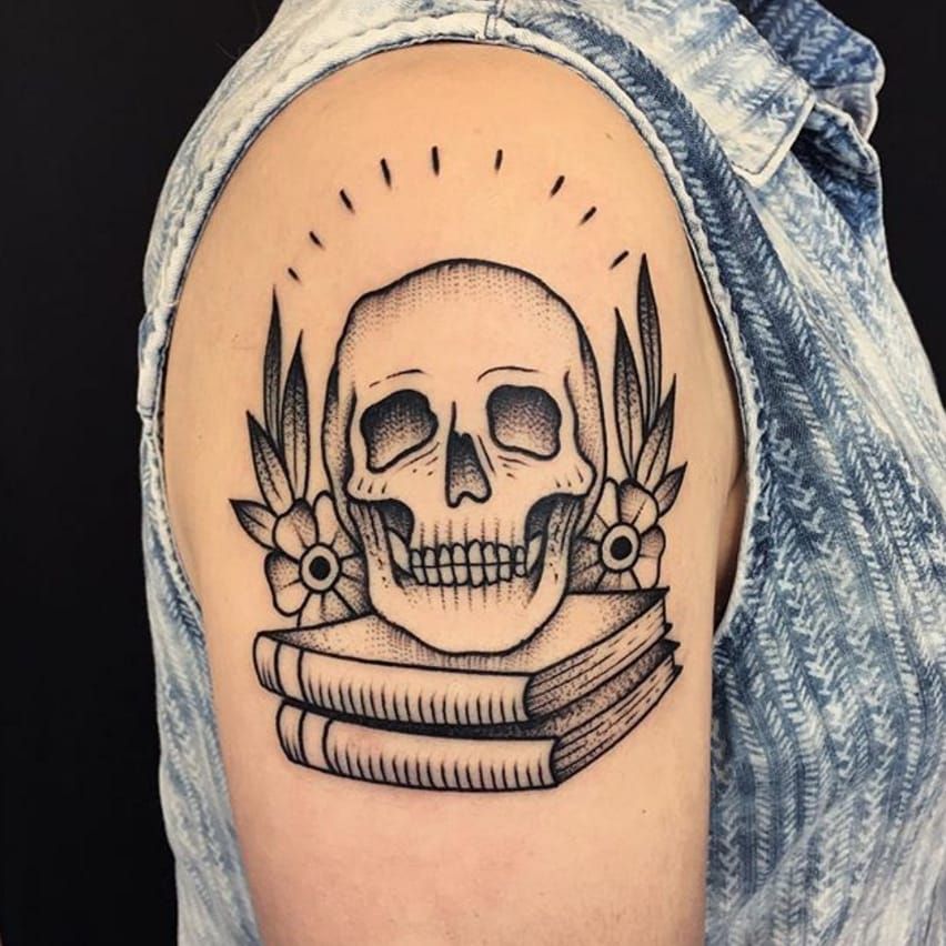 Grey shaded traditional skull with books and flowers tattoo on upper arm
