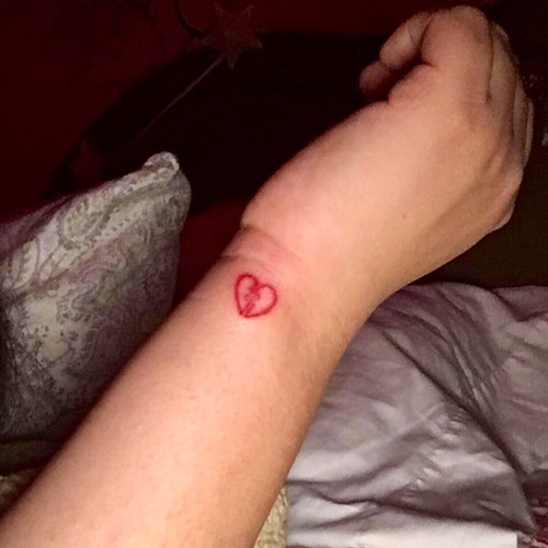 Red small broken heart tattoo on left upper hand wrist