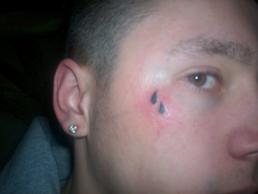 Black filled teardrop tattoo below right eye for men