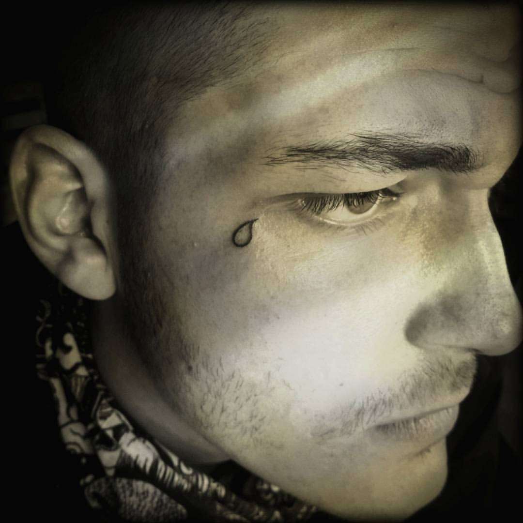 Black unfilled teardrop tattoo near right eye for men