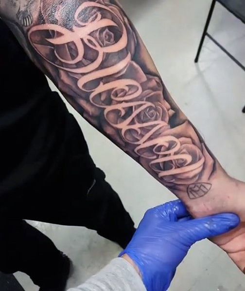 Black shaded roses with simple blessed tattoo on inner full forearm