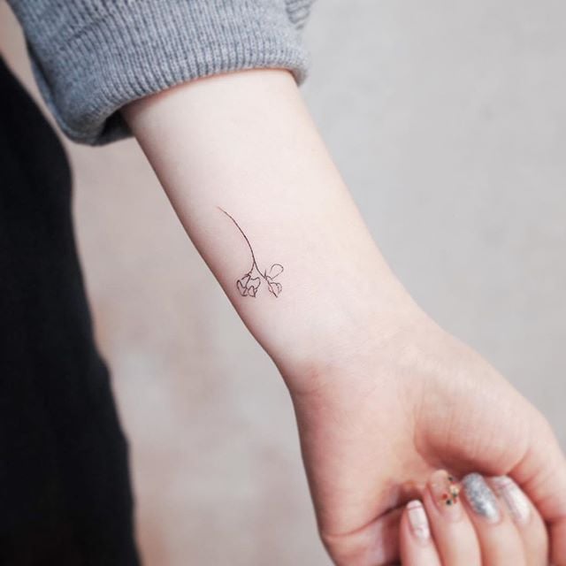 Black outlined small rose tattoo on left inner forearm for women