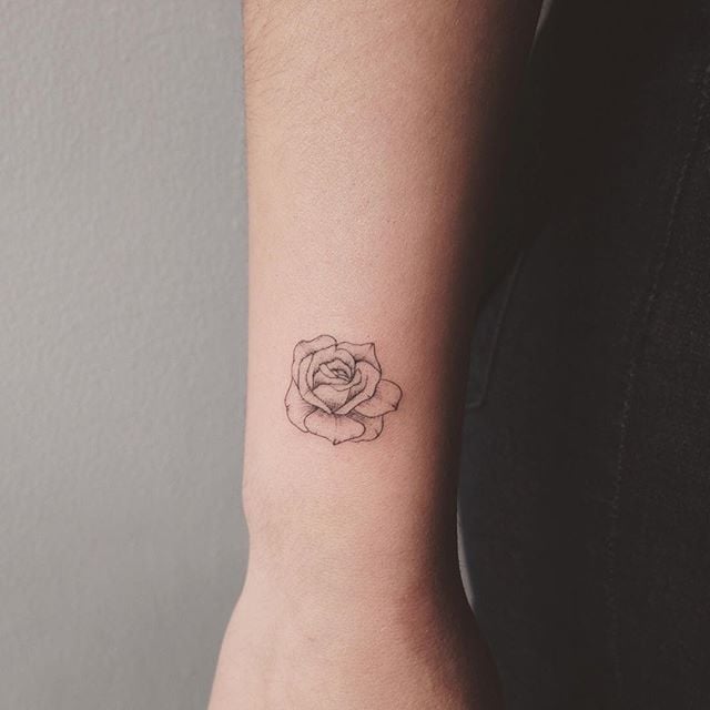 Black small rose tattoo on forearm